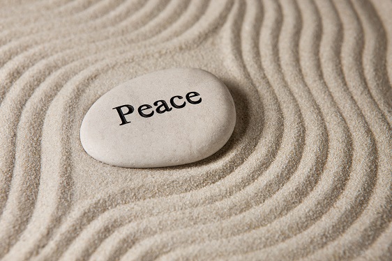 A stone with the word "peace" printed on it, in the middle of sand which is raked around the stone