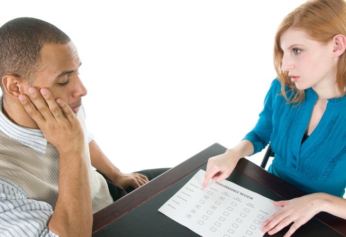 Photo of a man and women at a desk with a piece of paper that says performance review