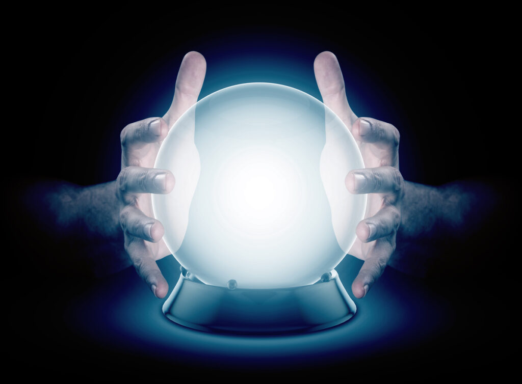 A pair of male hands surrounding a crystal ball conjuring up a hologram on an isolated dark studio background