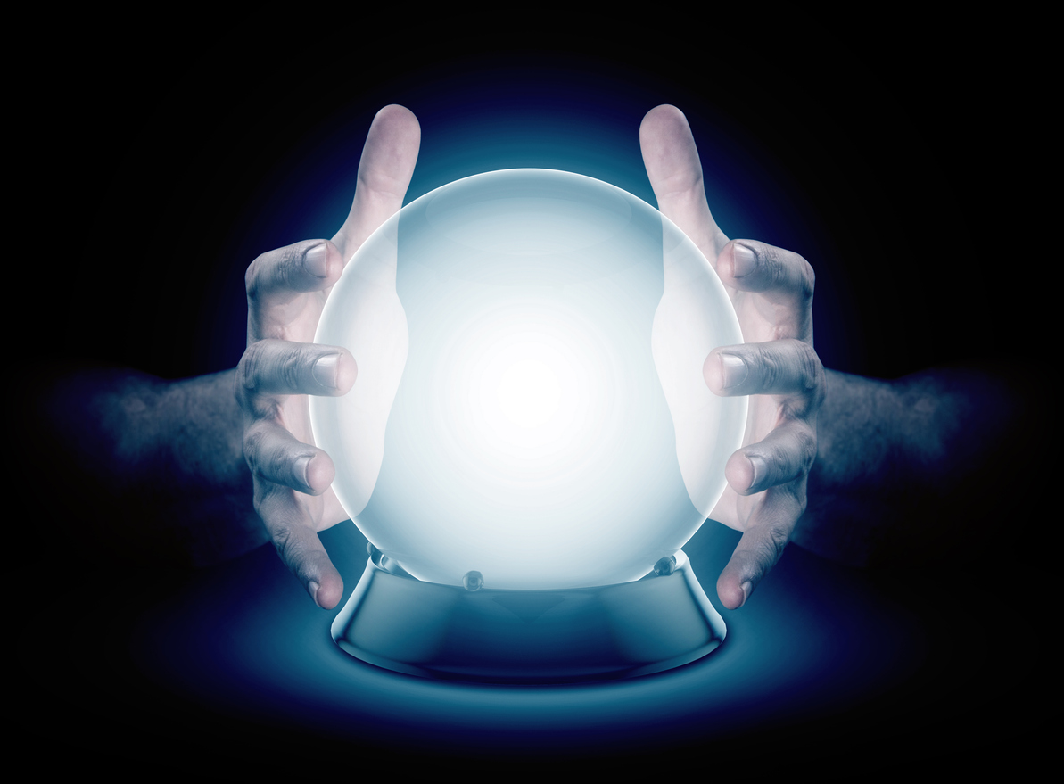 A pair of male hands surrounding a crystal ball conjuring up a hologram on an isolated dark studio background