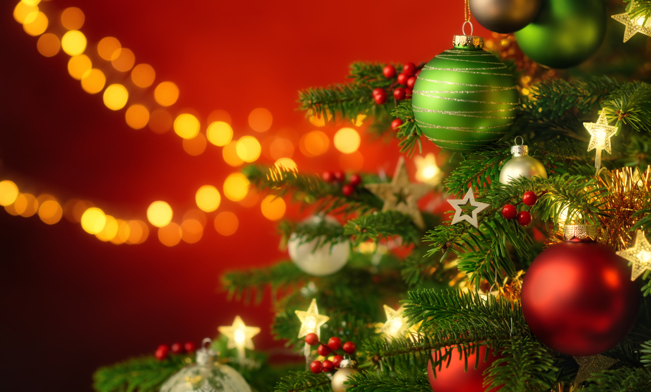 Festive happy Christmas scene with the closeup of a nicely decorated fir tree and red illuminated background with hanging blurred lights