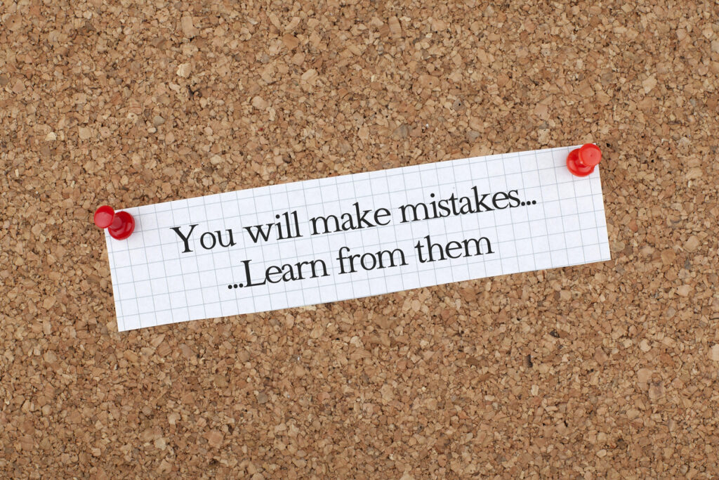 A corkboard with a note pinned on it using 2 red push pins. The note says "You will make mistakes... learn from them."