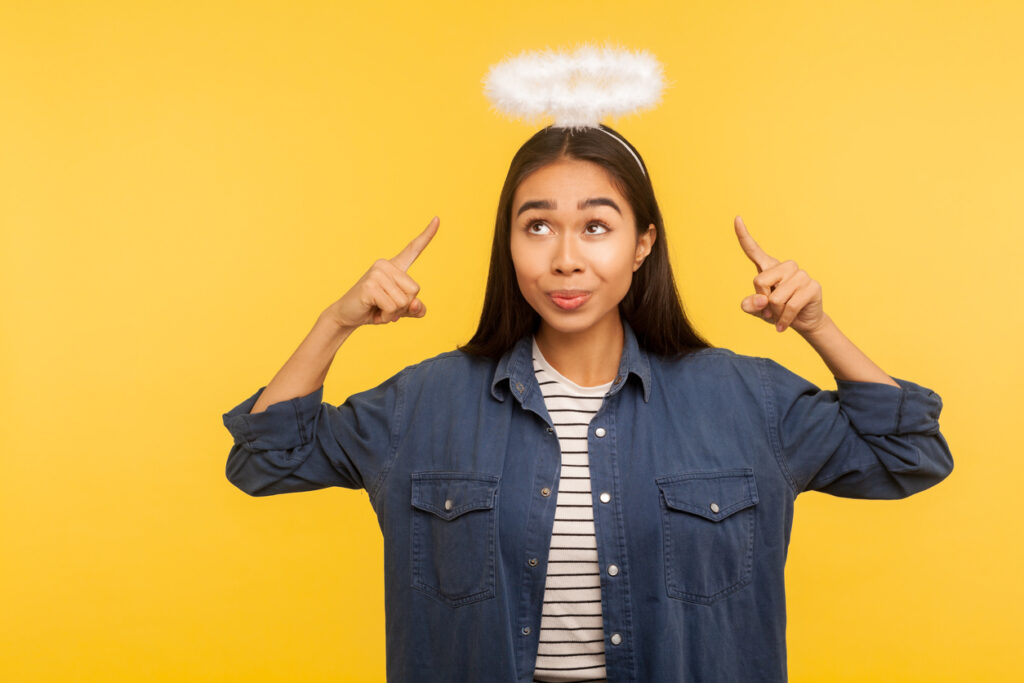 A yellow background with a woman pointing to the white halo she is wearing on her head