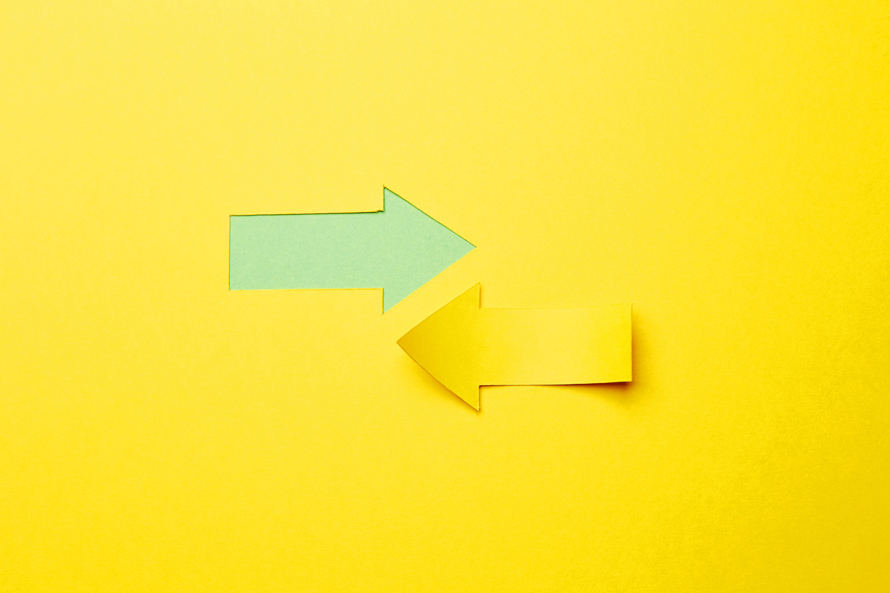 Two opposite left/right arrows, one cutted from the yellow paper curved up of two sides on the yellow paper background other made as an arrow shaped hole in the background with green paper underlay