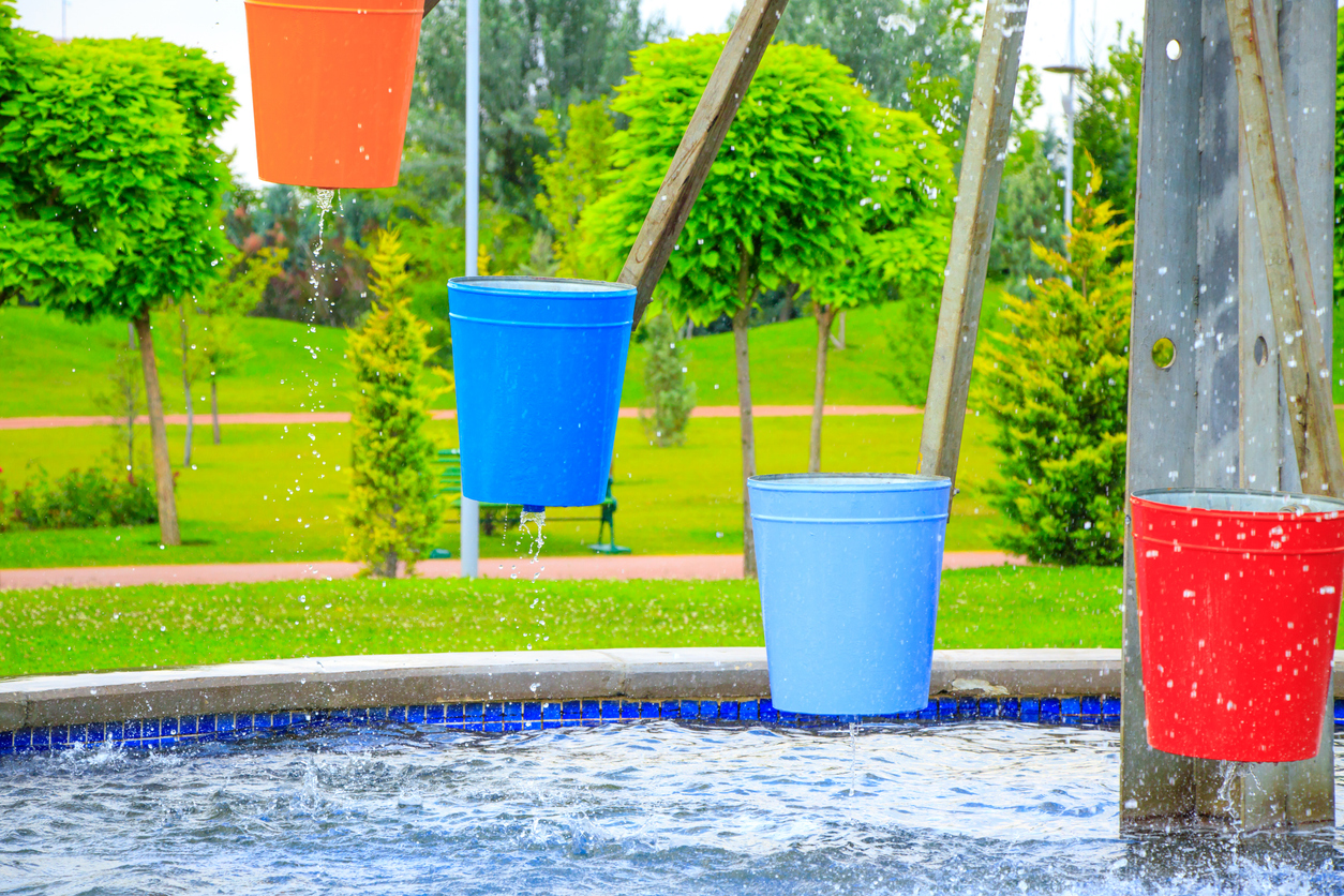 A partial view of a waterwheel with colorful buckets set against a bright outdoor background