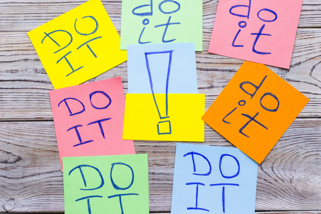 Sticky colorful notes inscribed with "do it" words with an exclamation mark in the middle, top view. Light wooden background. Business and motivation concept.