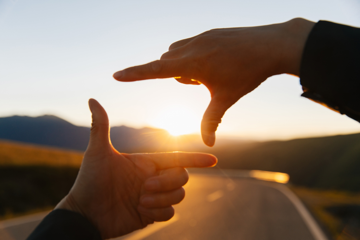 Hands in the shape of a picture frame against the sunset