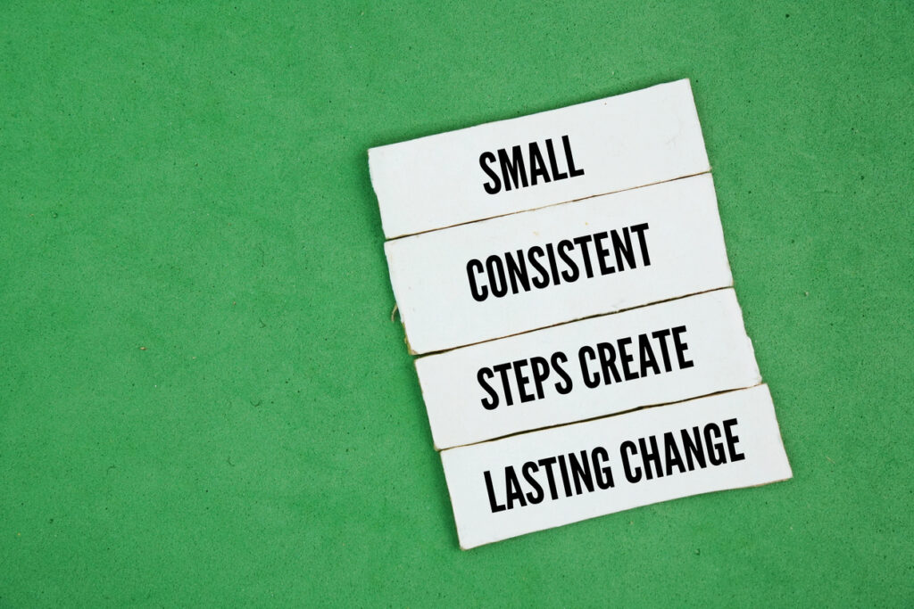 A green background with the words "small consistent steps create lasting change" on white paper in black text