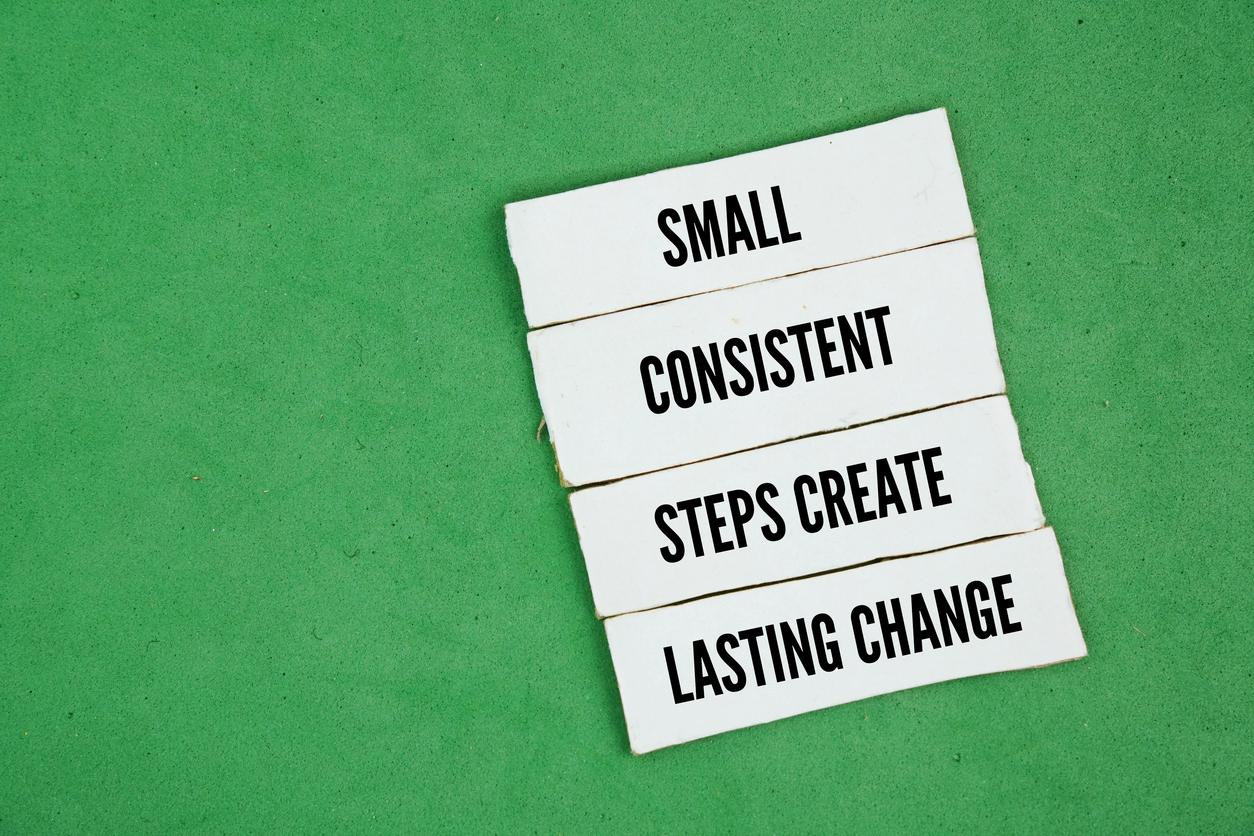 A green background with the words "small consistent steps create lasting change" on white paper in black text
