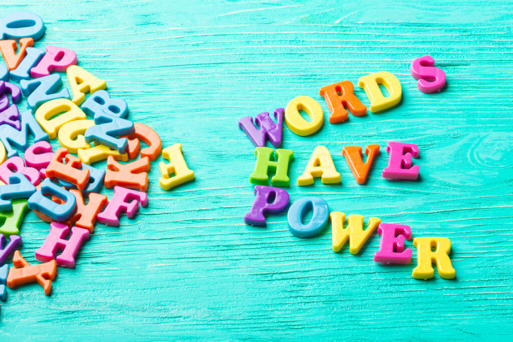 Colorful plastic alphabet letters are scattered across a turquoise wooden surface, with a random pile on the left and the words "WORDS HAVE POWER" arranged on the right.
