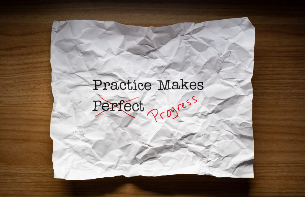 Image of crumpled piece of paper with the words "practice makes perfect" with the word "perfect" crossed out and replaced with the word "progress"