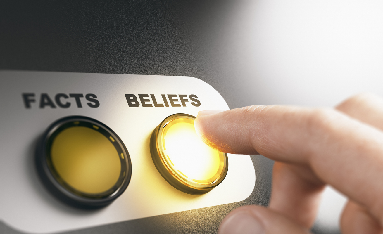 A hand presses a glowing button labeled “BELIEFS,” beside a darker button labeled “FACTS.”