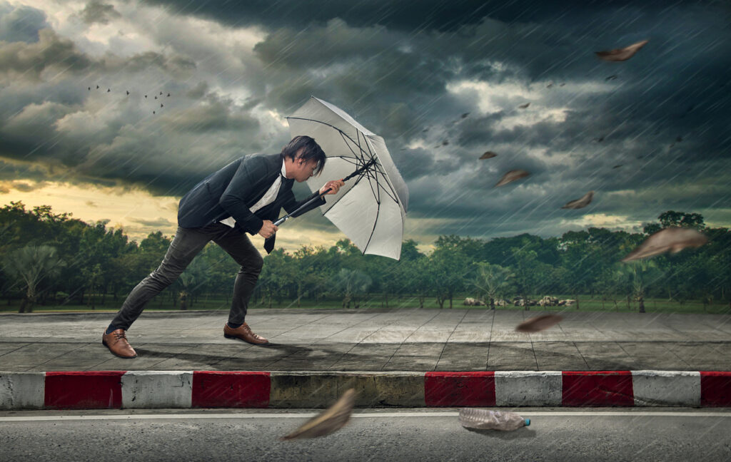 A businessman struggles against fierce wind and rain while holding onto a battered umbrella, symbolizing adversity and perseverance.