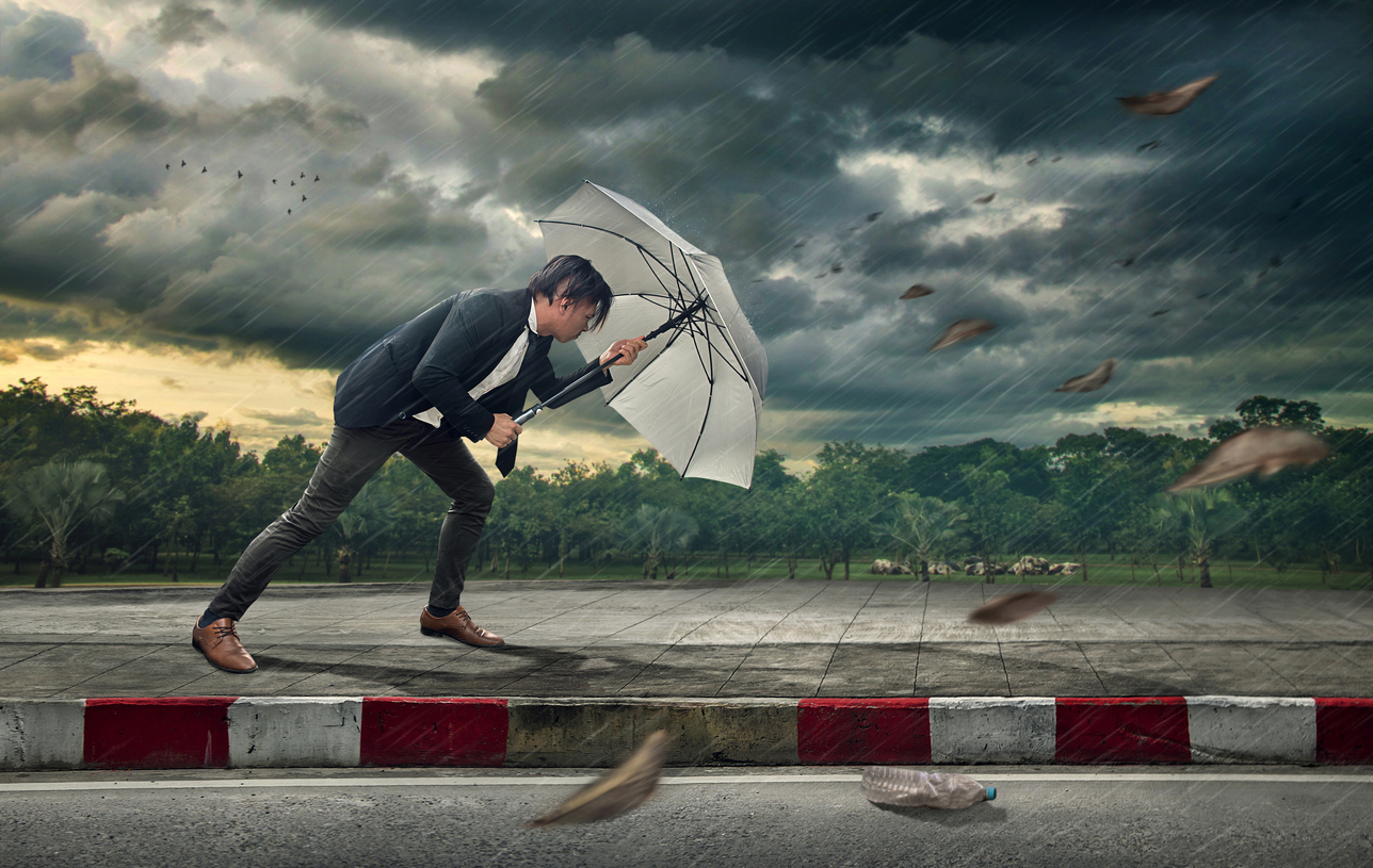 A businessman struggles against fierce wind and rain while holding onto a battered umbrella, symbolizing adversity and perseverance.