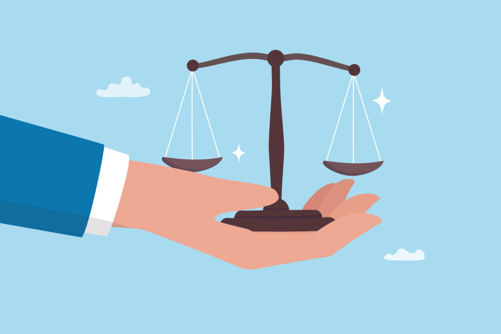 A flat illustration of a hand holding a balanced set of scales of justice against a light blue background, symbolizing fairness, objectivity, and impartial judgment.